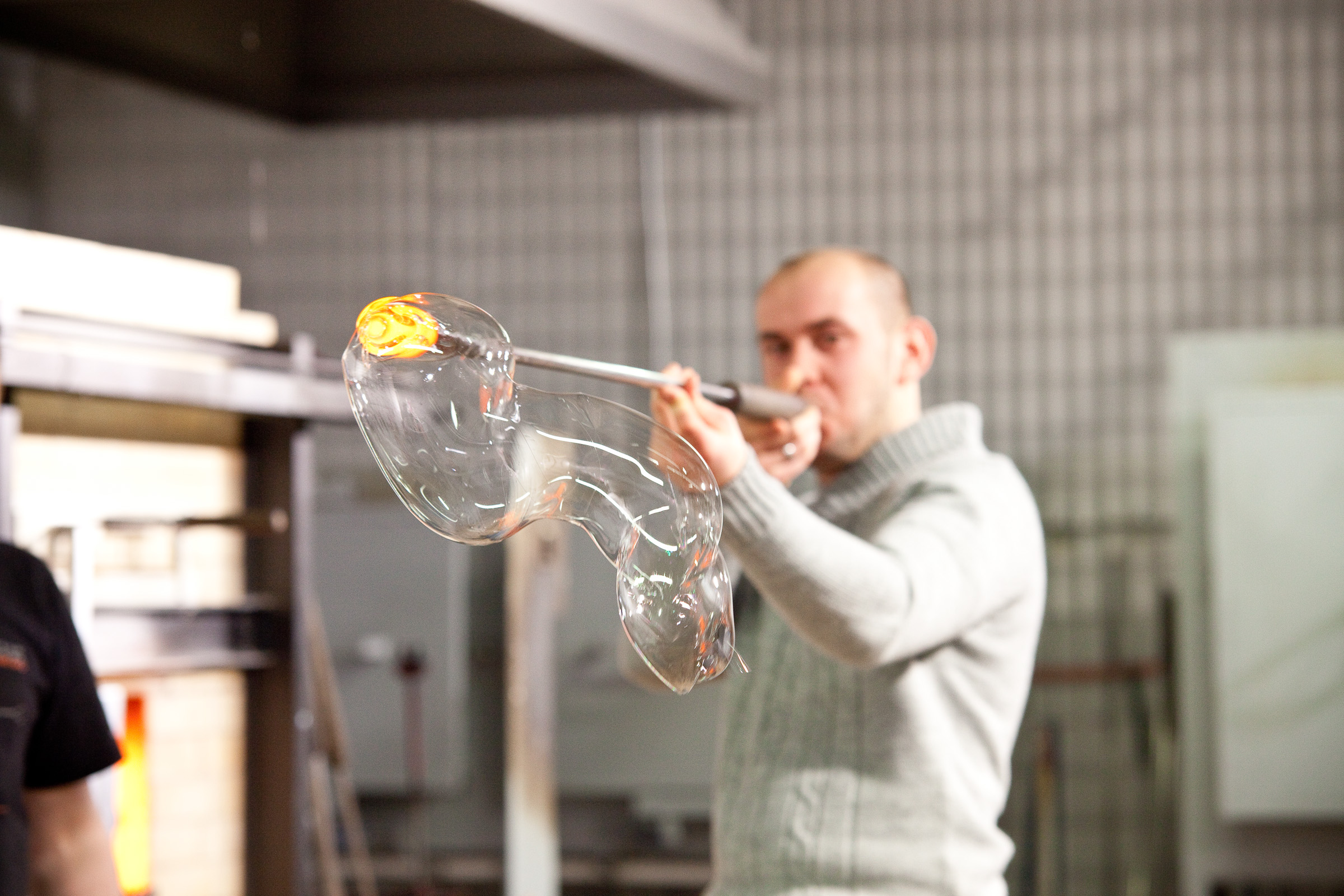 Mężczyzna wydmuchujący przez długą metalową rurkę kształt z rozgrzanego szkła.