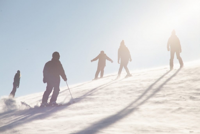 Zima. Sylwetki narciarzy zjeżdżających ze stoku w promieniach słońca.
