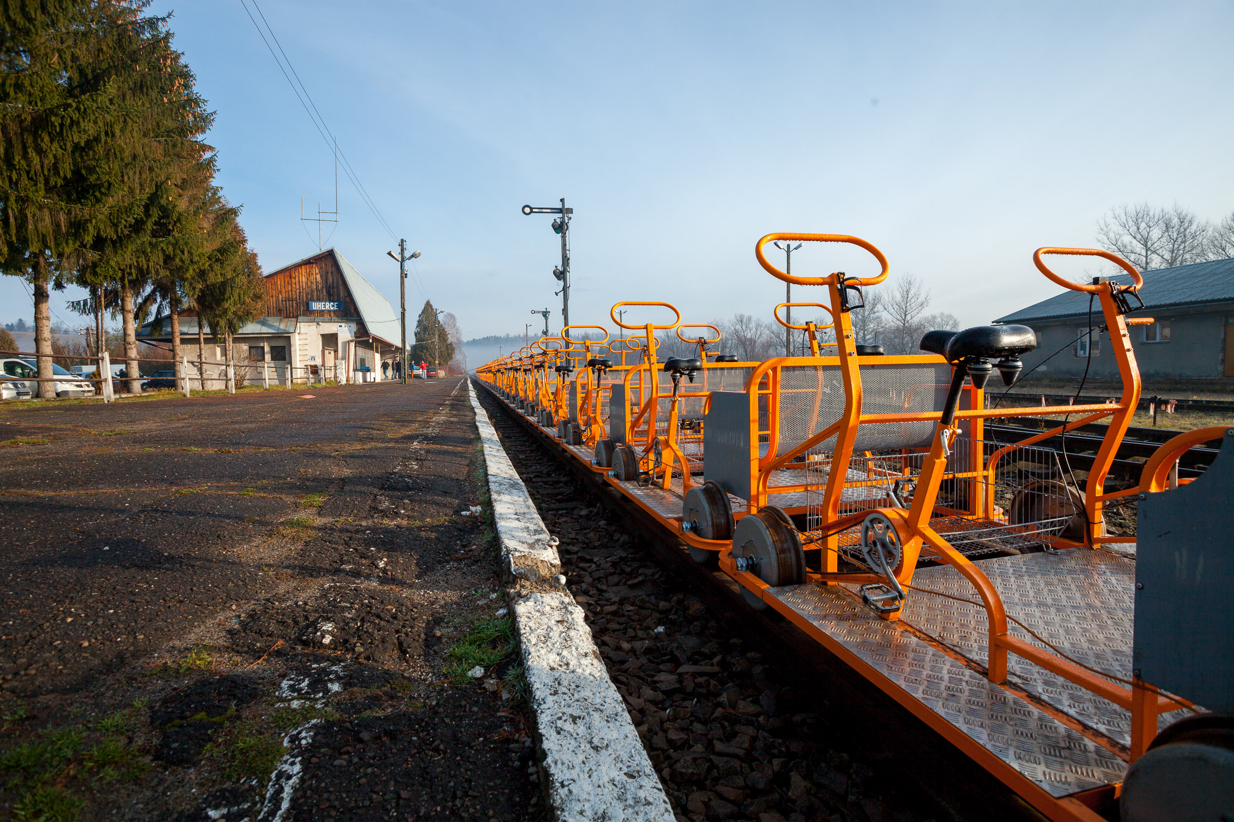 Pomarańczowe drezyny rowerowe ustawione na torach na stacji w Uhercach. W tle budynek dworca.