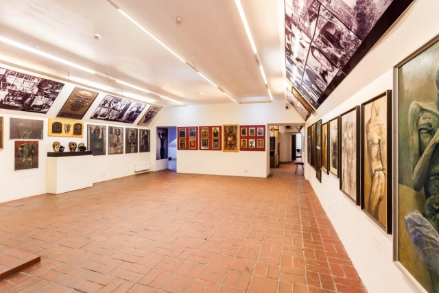 Sala wystawowa. Na ścianach zawieszone obrazy i zdjęcia Beksińskiego. W pomieszczaniu jest jasno.