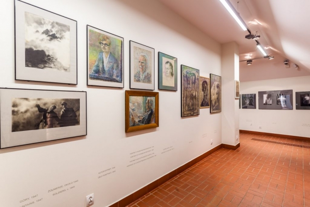 Sala wystawowa. Na ścianach zawieszone obrazy i zdjęcia Beksińskiego. W pomieszczaniu jest jasno.