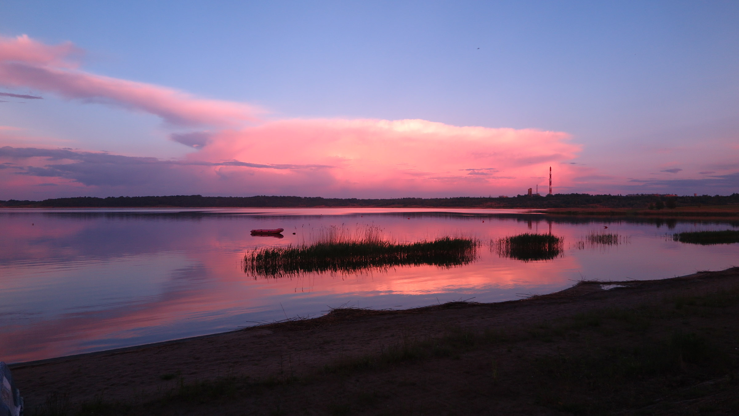 Zachód słońca nad jeziorem. Purpurowe niebo odbija się w tafli jeziora.