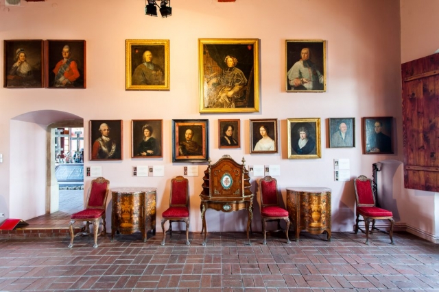 Sala portretowa. Na ścianie umieszczone portrety. W sali znajdują się zabytkowe meble: fotele i drewniane, bogato zdobione komody i sekretarzyk.