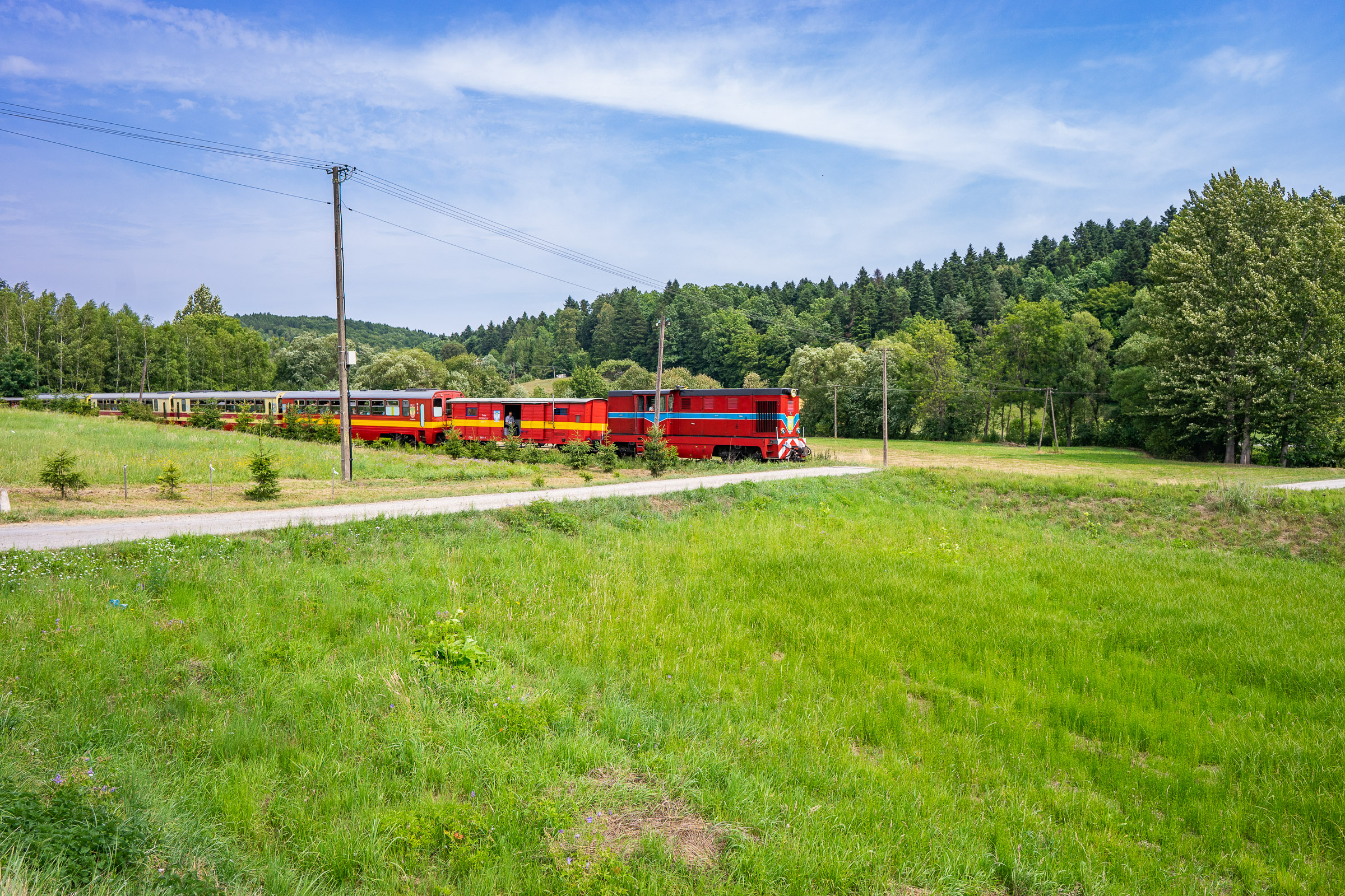 Czerwona lokomotywa ciągnąca skład z wagonami.