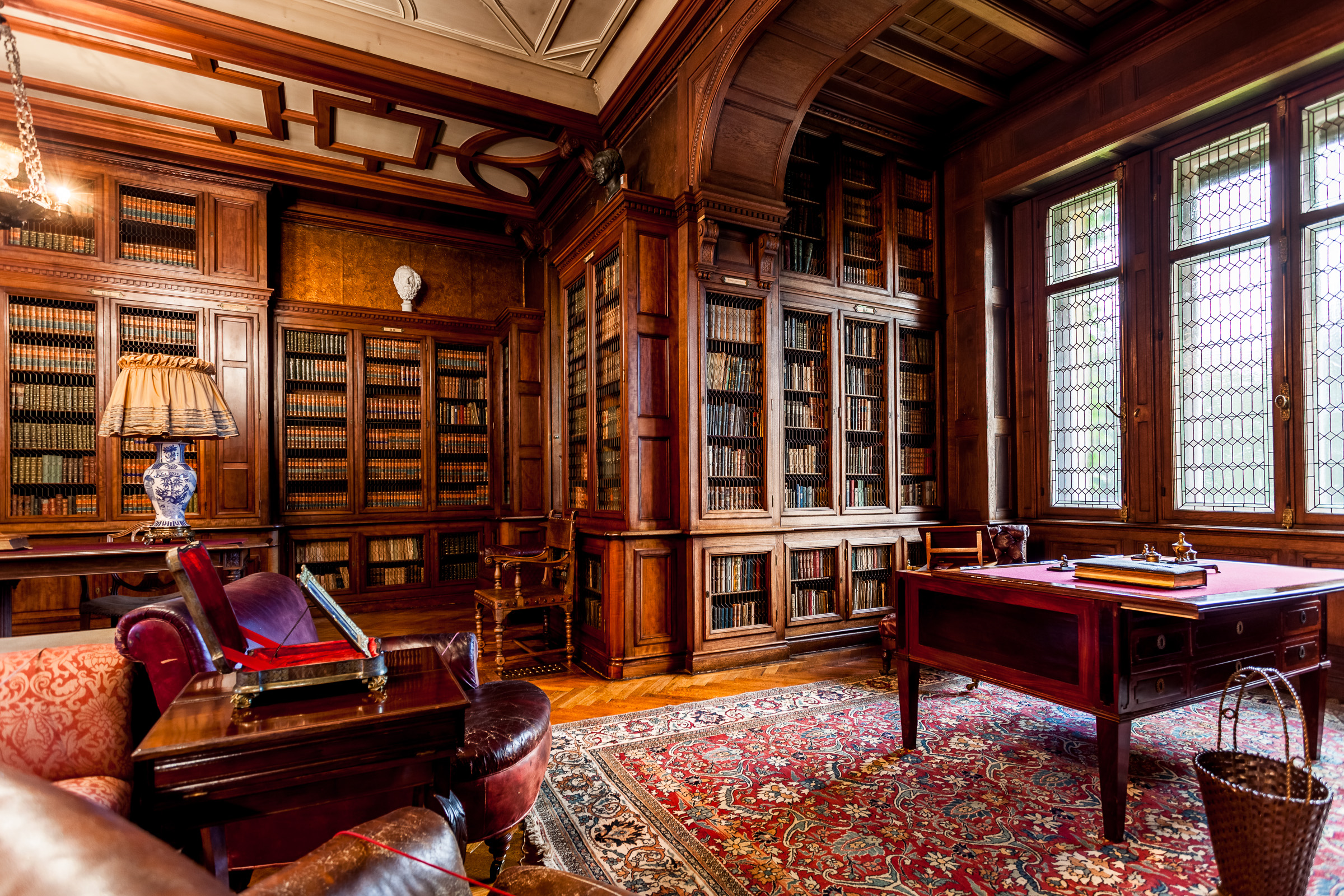 Eleganckie wnętrze w stylu angielskim. Na środuku sofa i skórzane fotele. Przy ścianach drewniane, zdobione regały z książkami.