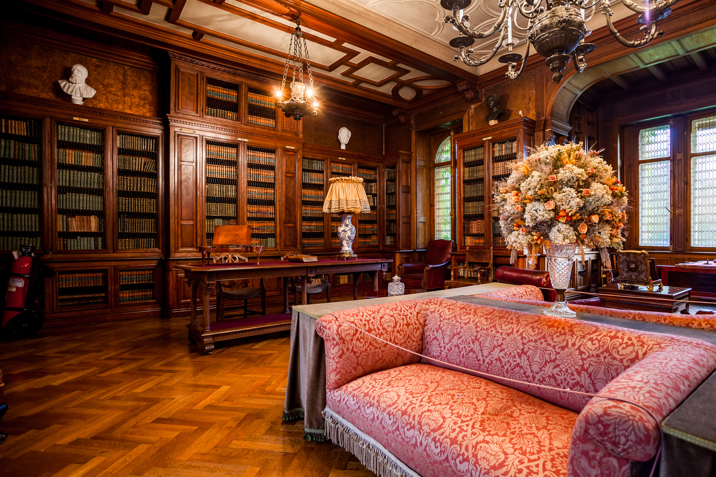 Eleganckie wnętrze w stylu angielskim. Na środuku sofa. Przy ścianach drewniane, zdobione regały z książkami.