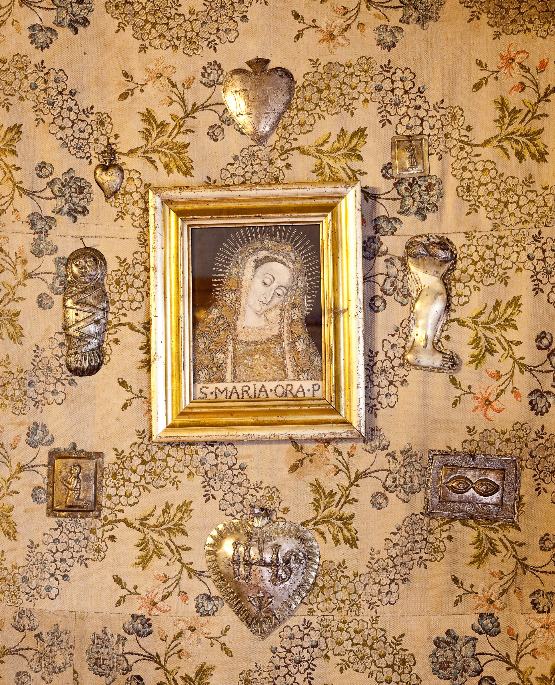 Detal. Obrazek Matki Boskiej w złotej ramce. Obok srebrne ozdoby z symbolami religijnymi