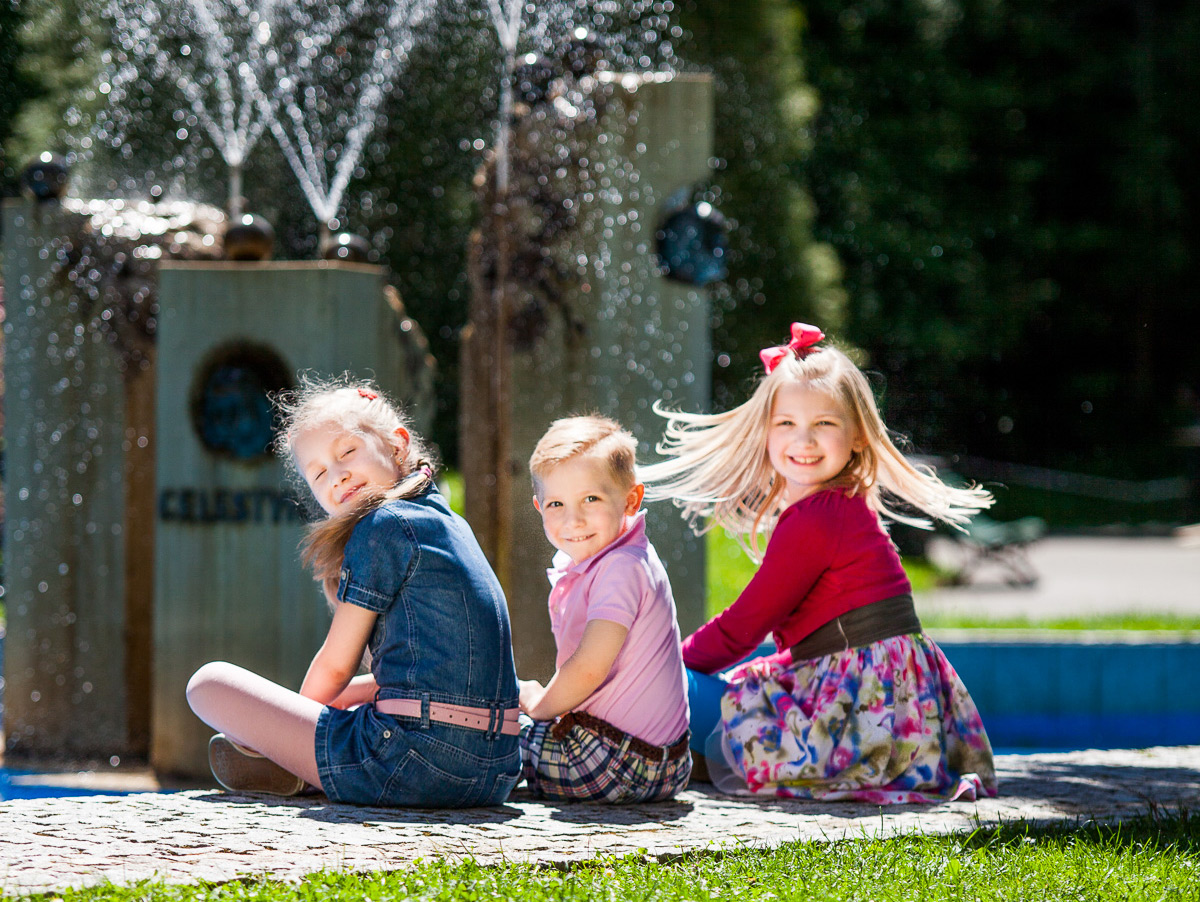 Trójka uśmiechniętych dzieci. W tle fontanna.