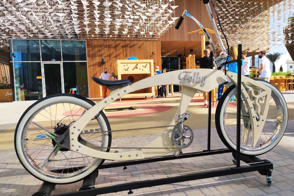 Dizajnerski rower marki Folky ustawiony przed Pawilone Polski w Dubaju. W tle grupa osób.