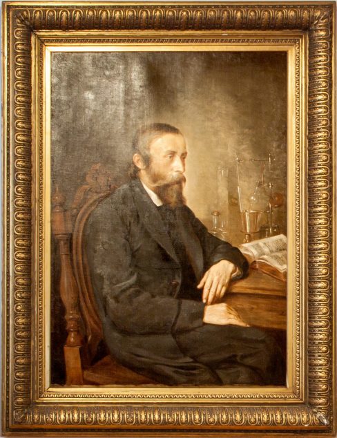 Portret Łukasiewicza, mężczyzny w średnim wieku, z brodą i wąsami. Dominują kolory brązowe. Obraz oprawiony w złotą ramę.