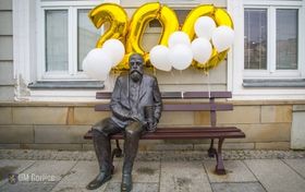 Posąg Ignacego Łukasiewicza siedzącego na ławce. Pomnik przyzdobiony białymi balonami i złotymi balonami w kształcie cyfr 200.