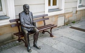 Pomnik z brązu. Ignacy Łukasiewicz, mężczyzna z brodą siedzący na ławce. W ręku trzyma lampę naftową. Pomnik umieszczony na ławce, na której można usiąść.