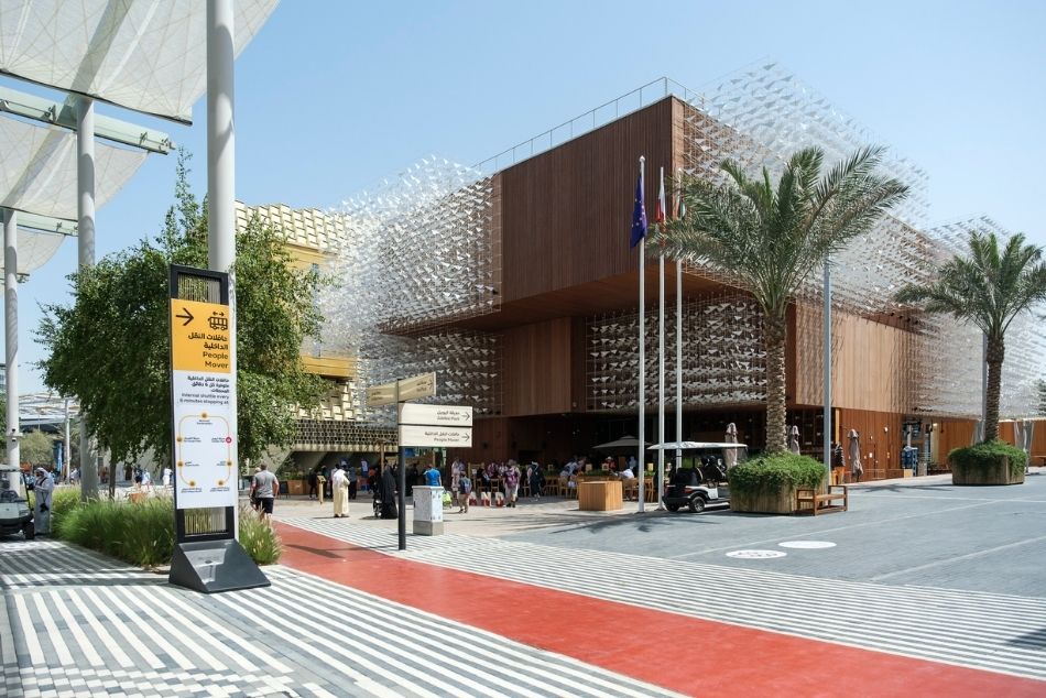 Zdjęcie Pawilonu Polskiego na EXPO w Dubaju. Drewniany, kilkupiętrowy budynek, o nowoczesnej, geometrycznej bryle pokryty ażurową rzeźbą kinetyczną symbolizującą ptaki w locie.