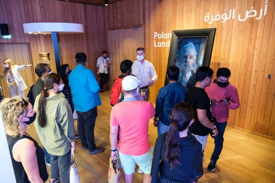Grupa osób zwiedzająca wystawę. W tle portret Ignacego Łukasiewicza.