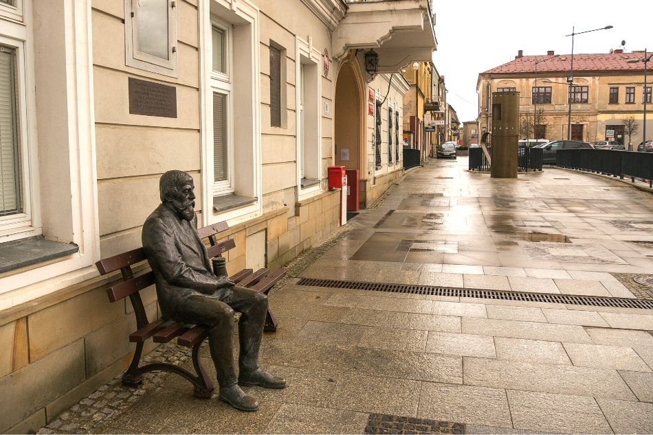 Rynek miasta, przy kamienicy znajduje się ławka z posągiem siedzącego Ignacego Łukasiewicza, starszego mężczyny trzymającego w ręku lapmę naftową. Na ławce jest miejsce, aby usiąść obok. W dalszej części zdjęcia znajduje się kilkumetrowy model pierwszej na świecie lampy naftowej.