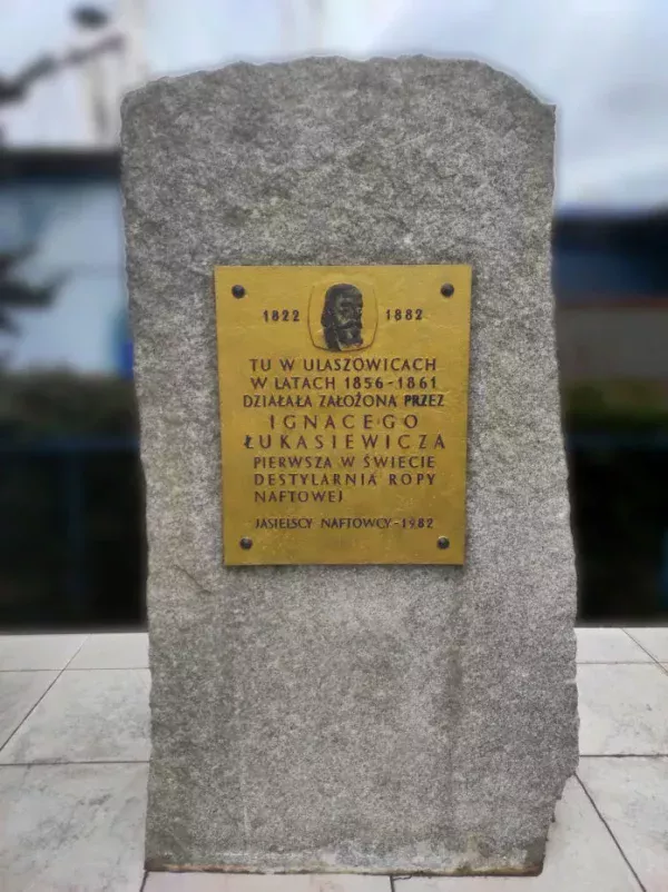Kamienny obelisk z tablicą o treści: Tu w Ulaszowicach w latach 1856 - 1861 działała założona przez Ignacego Łukasiewicza pierwsza w świecie destylarnia ropy naftowej. Jasielscy naftowcy - 1982.