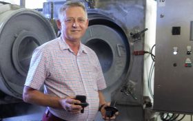 Mężczyzna w śrenim wieku w koszuli z krótkim rękawem stoi na tle urządzeń produkcyjnych w fabryce