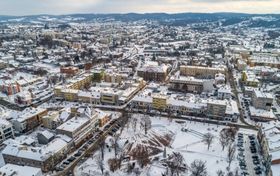 Zimowa panorama miasta z lotu ptaka. Kilkupiętrowe kamienice i bloki, w oddali wzgórza.