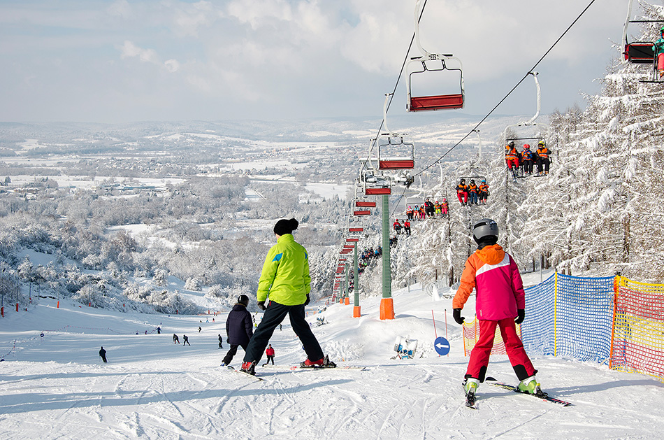 Wyciąg narciarski zimą. Narciarze w jaskrawych kostuiumach zjeżdżają na nartach.