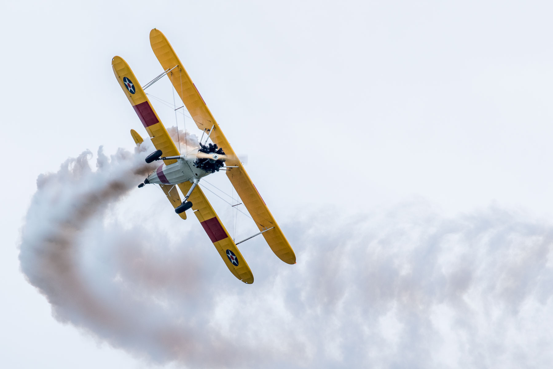 Dwupłatowy samolot wykonujący akrobację na niebie, za nim cięgnie się smuga dymu