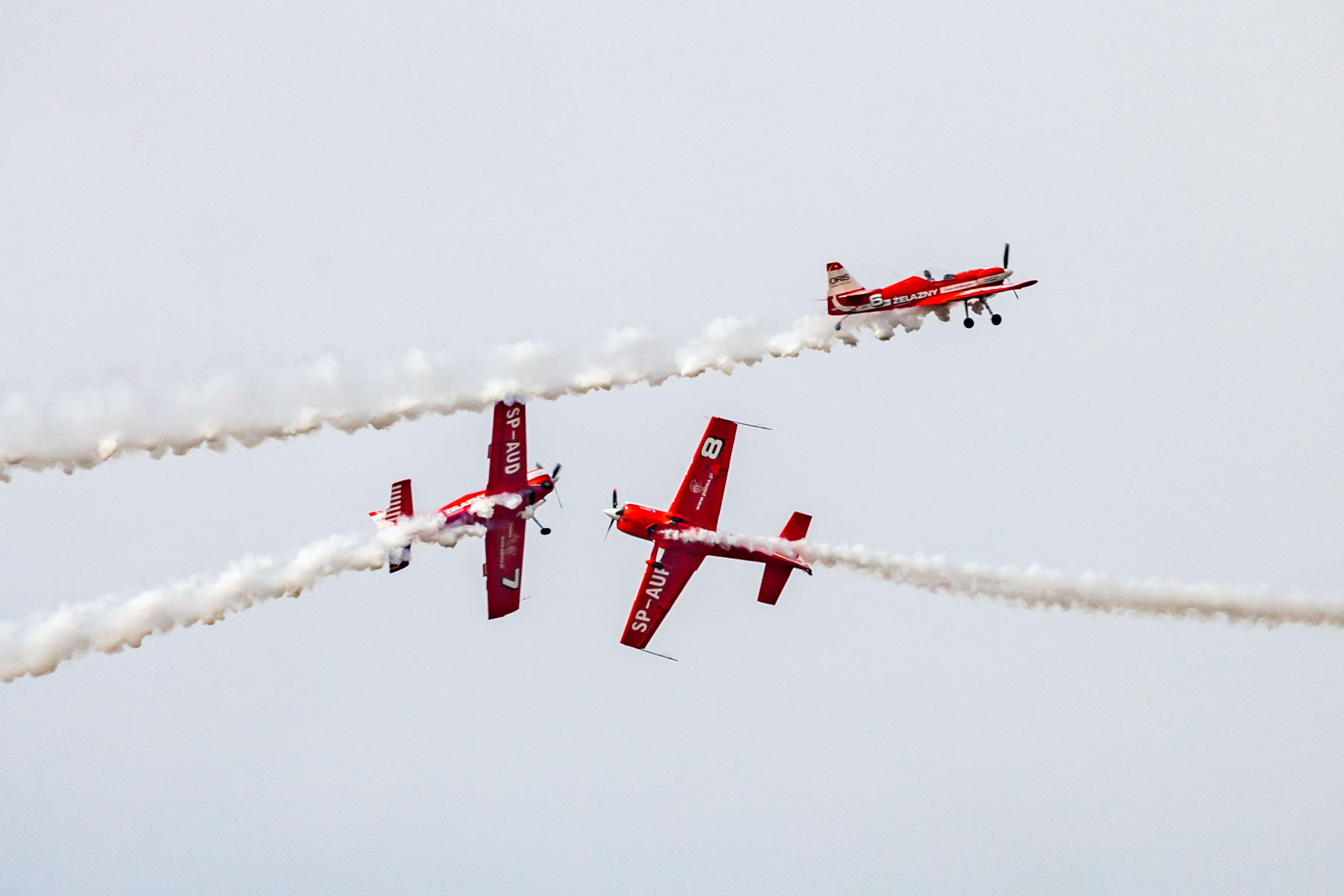 Trzy czerwone samoloty wykonujące podniebne akrobacje. Każdy z nich leci w innym kierunku.