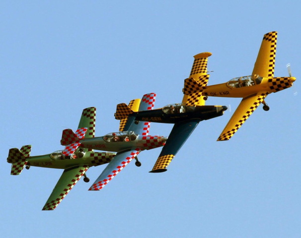 Cztery kolorowe samoloty lecące w szyku w bliskiej odległości, jeden za drugim.