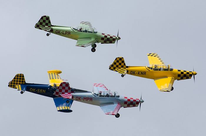 Cztery kolorowe samoloty lecące w szyku w bliskiej odległości.