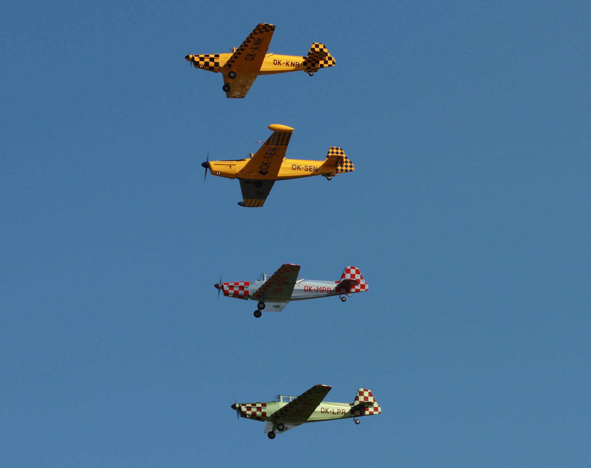 Cztery kolorowe samoloty lecące w szyku w bliskiej odległości, jeden nad drugim.