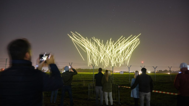 Publiczność oglądająca nocny pokaz dronów. Świecące drony lecą tworząc wrażenie spadających gwiazd.