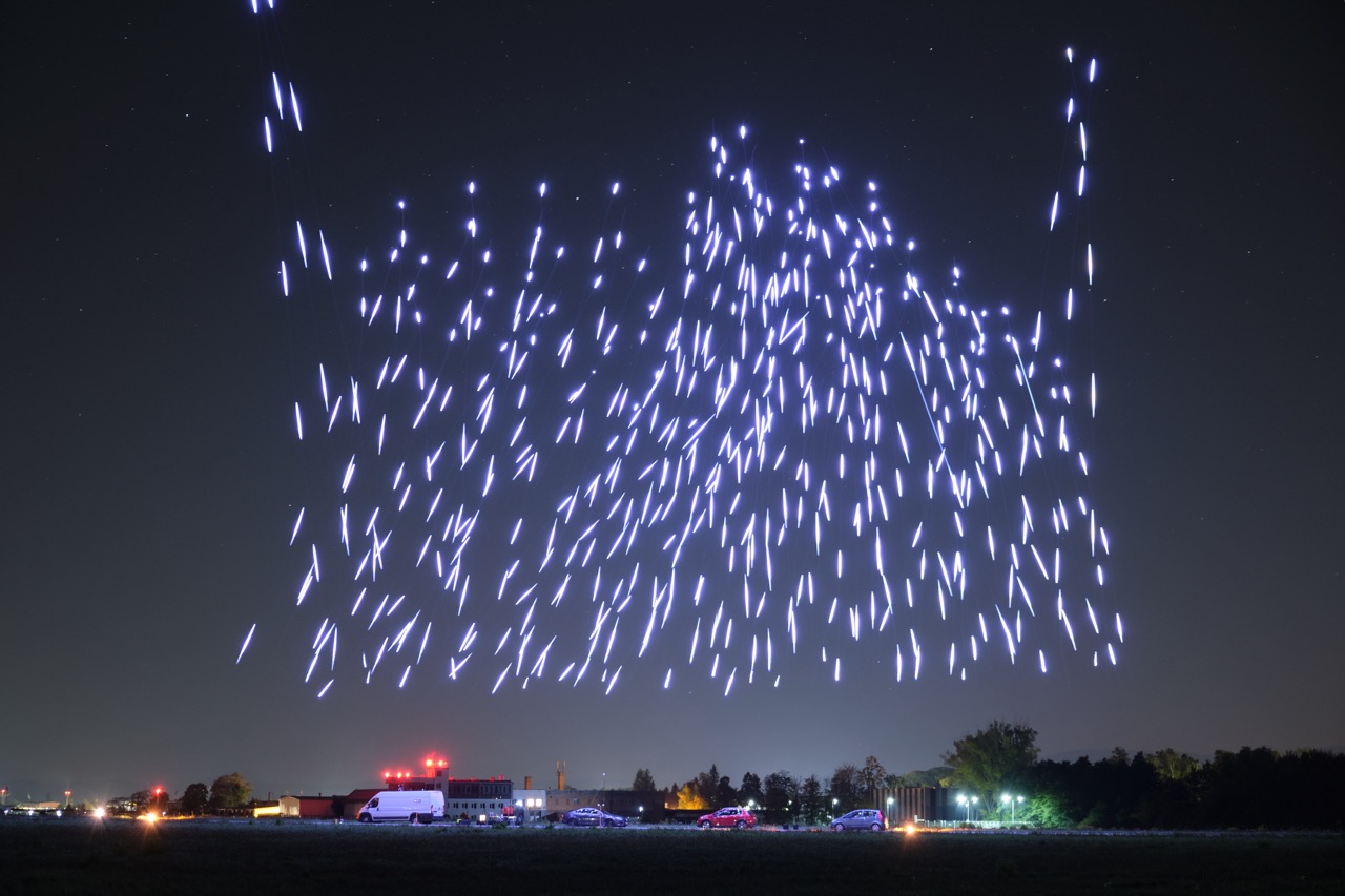Nocny pokaz dronów. Świecące drony lecą tworząc wrażenie spadających gwiazd.