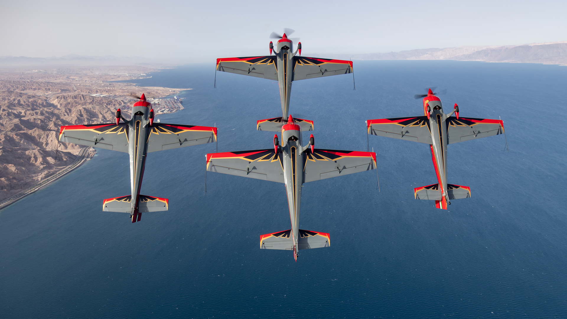 Cztery czerwone samoloty lecące w szyku w bliskiej odległości.
